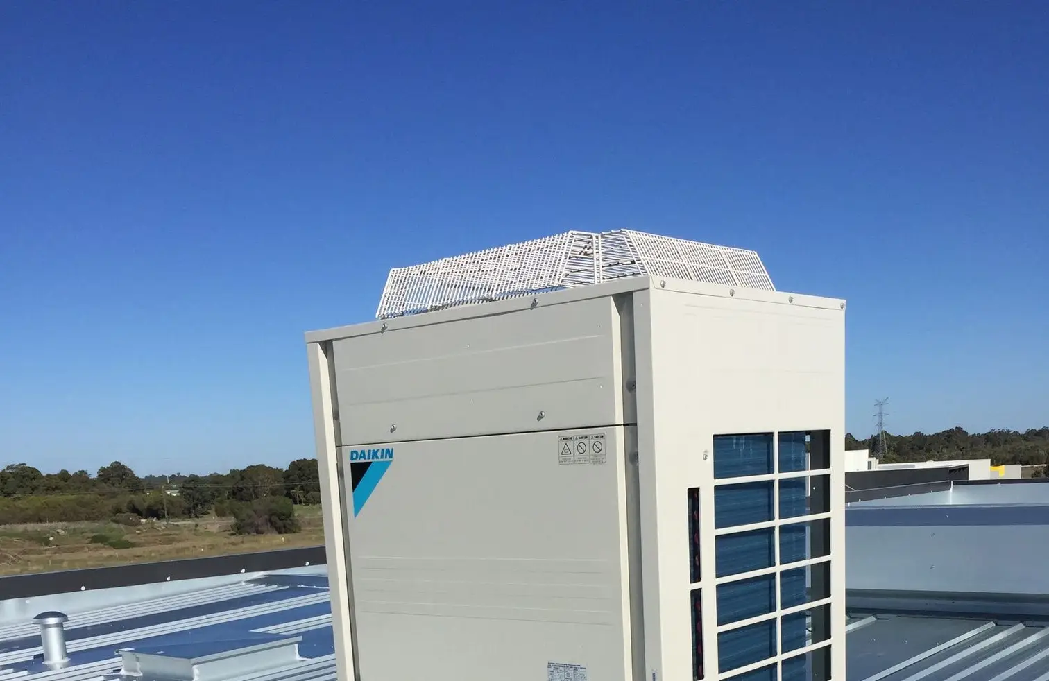 A Daikin outdoor condensing unit installed on a commercial metal roof under a clear Perth sky
