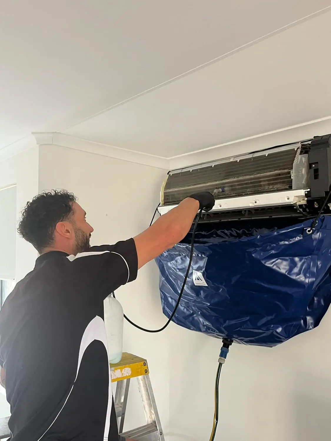 Aerobreeze technician washing out the coil of a wall split system indoors