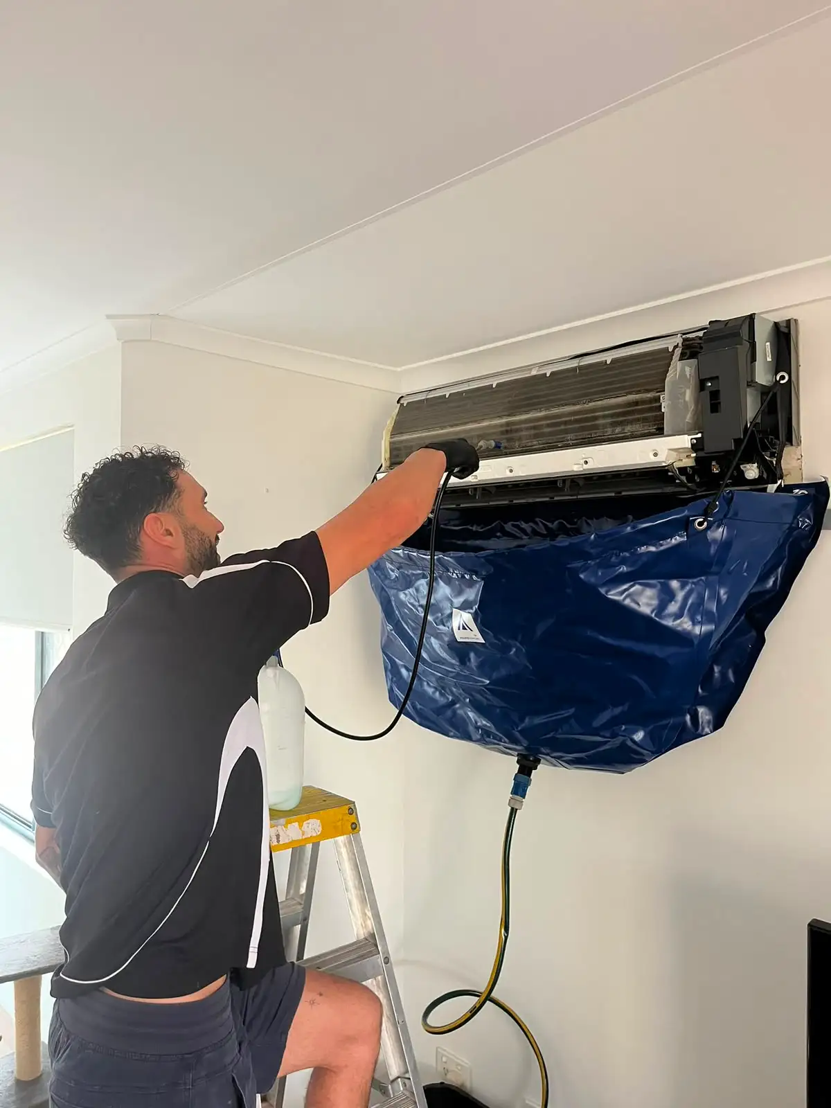 Aerobreeze technician on a step ladder washing out a wall split system, the wash bag hung beneath it